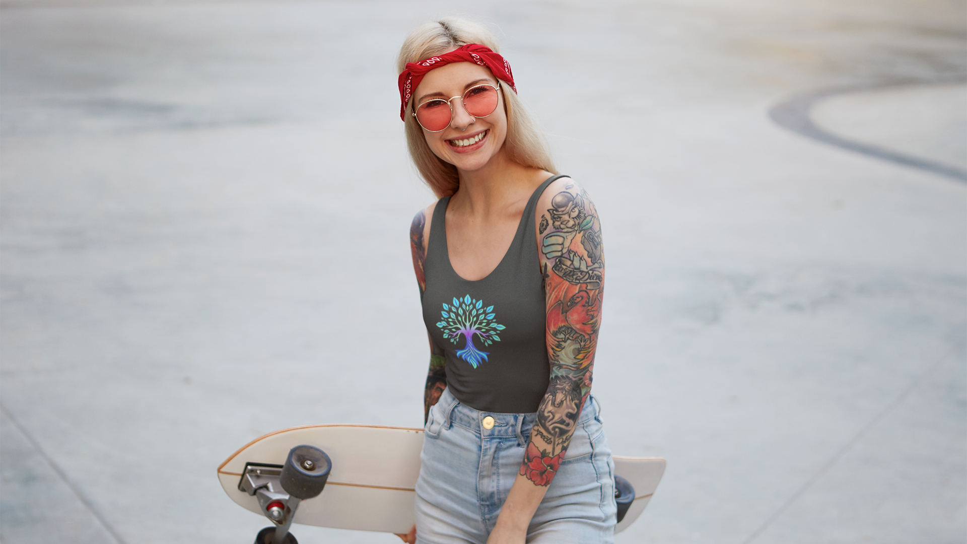 Woman with tattoos holding a skateboard, wearing a tank top with the Soul Art logo and denim shorts.