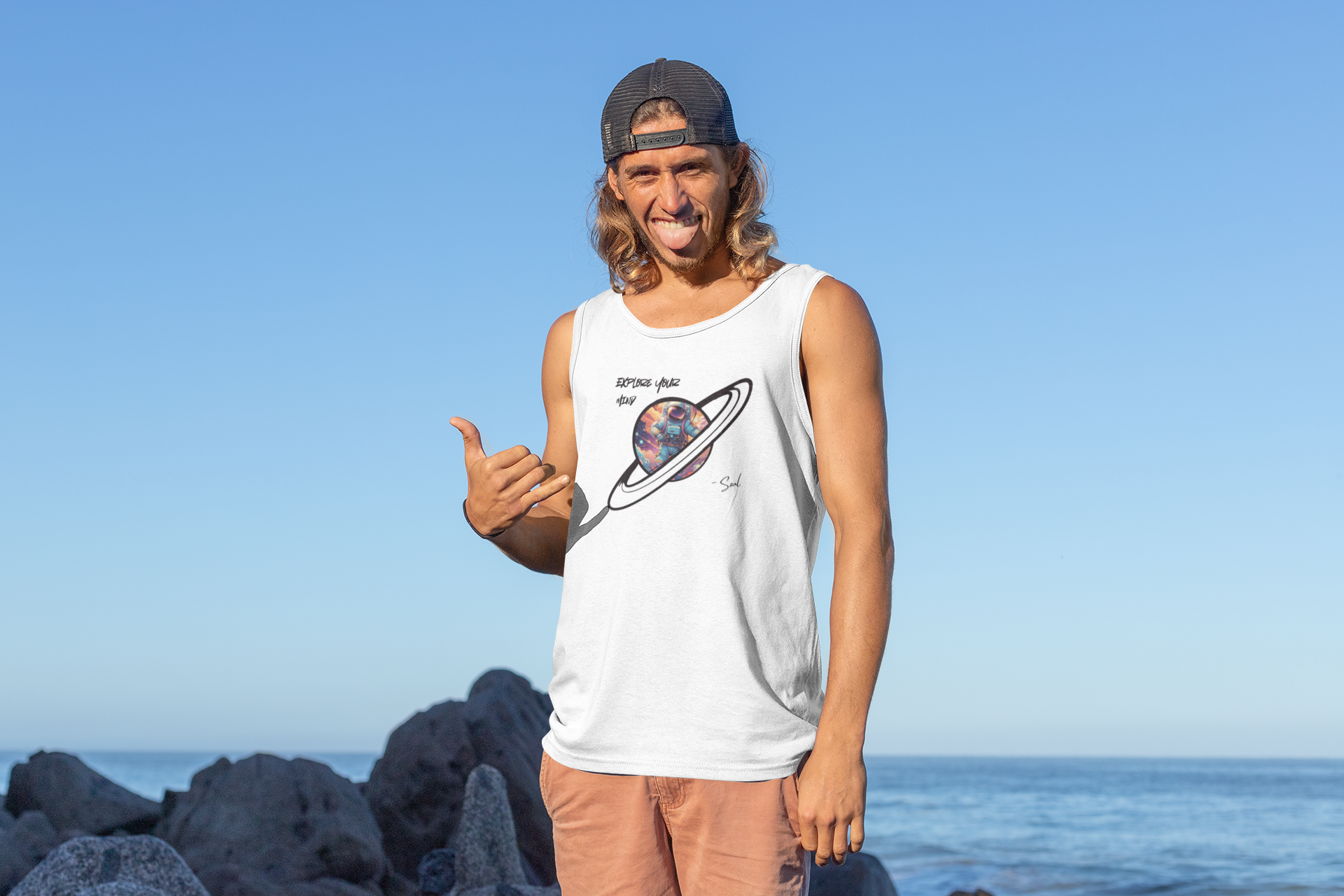Person wearing a sleeveless shirt with a graphic design by Soul Art, standing on rocks by the ocean.