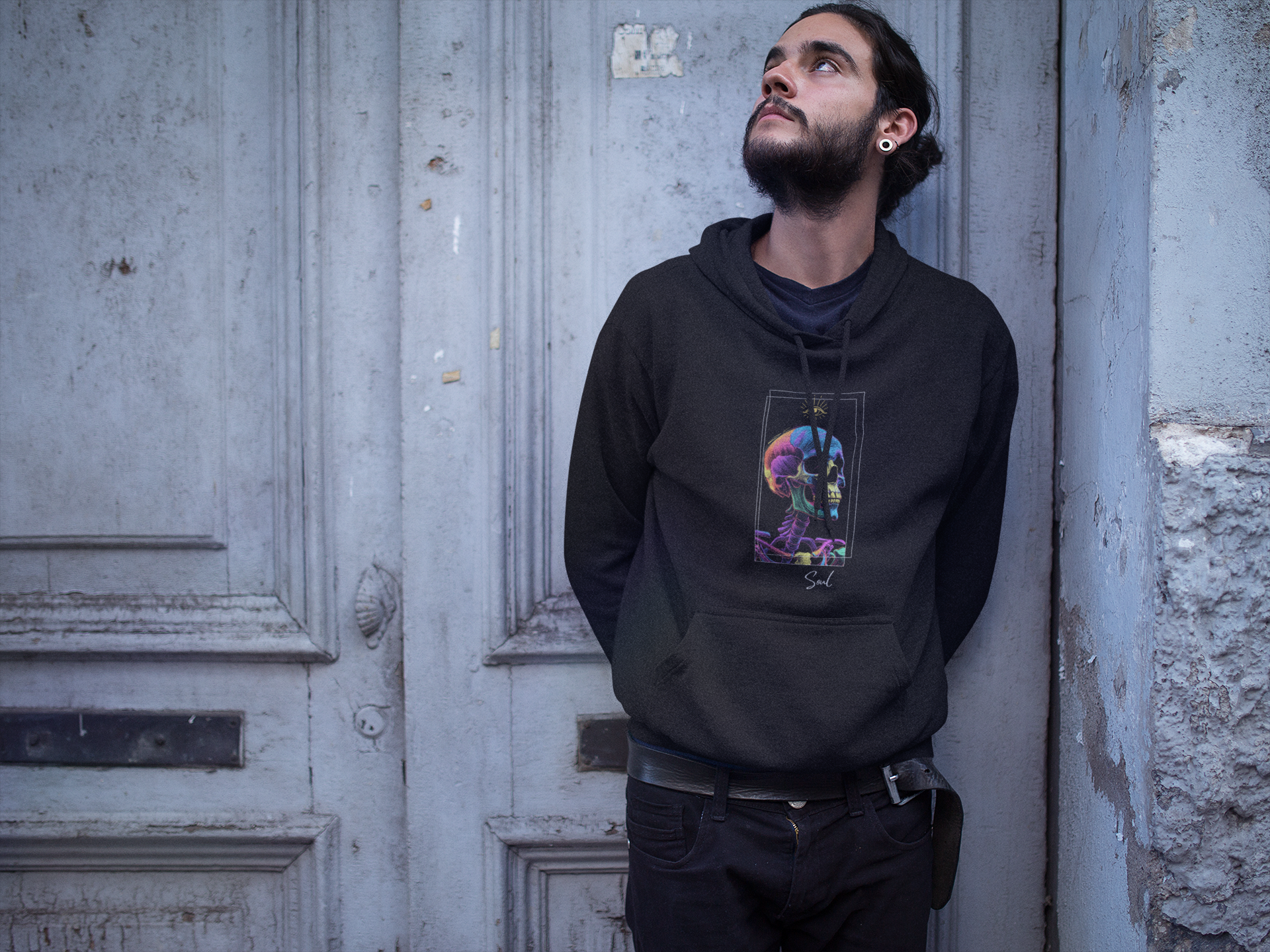 Dreaming Man wearing a black hoodie with the Soul Art colorful graphic design, leaning against a textured wall.